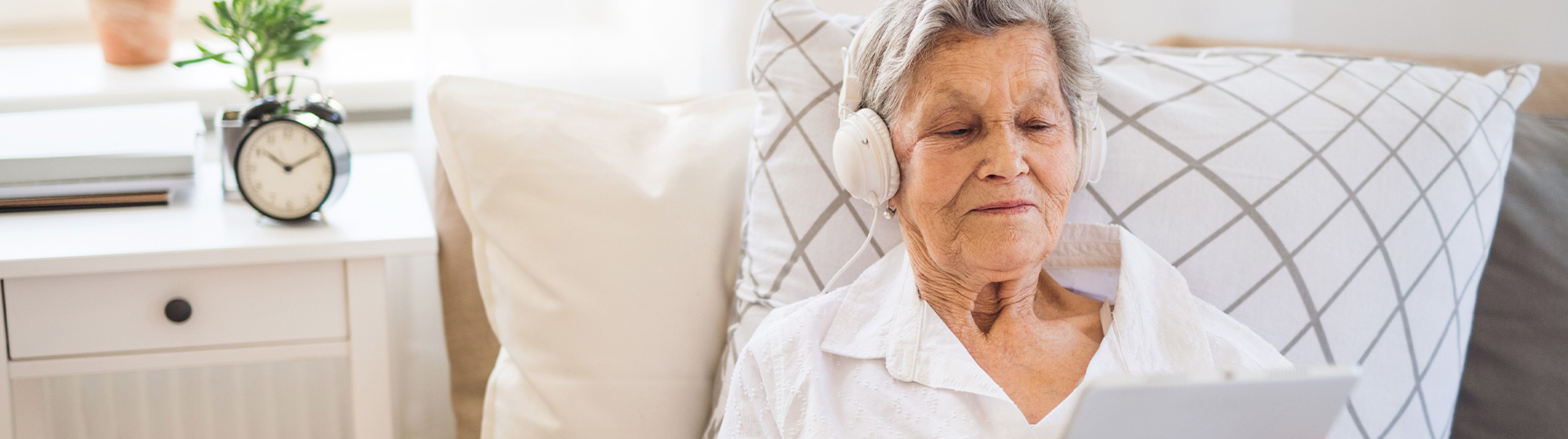 Ältere Dame sitzt mit Kopfhörern im Bett und hält Unterlagen in der Hand