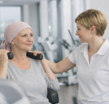 junge Frau mit Kopfbedeckung wird von einer Trainerin an einem Trainingsger&auml;t angeleitet