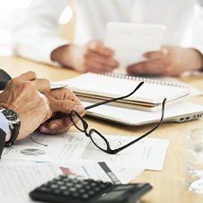 Bildausschnitt: Geschäftsleute an einem Tisch mit Brille, Taschenrechner und Unterlagen