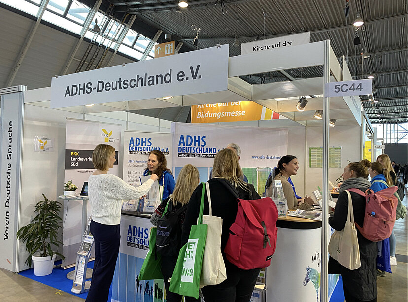Das Bild zeigt den Messestand des ADHS Deutschland e.V. mit vielen interessierten Besucherinnen und Besuchern davor.
