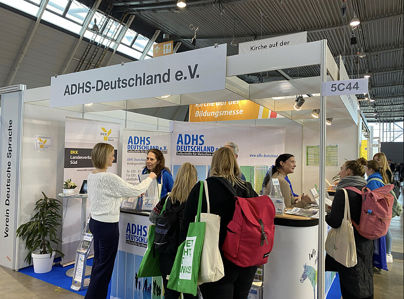 Das Bild zeigt den Messestand des ADHS Deutschland e.V. mit vielen interessierten Besucherinnen und Besuchern davor.