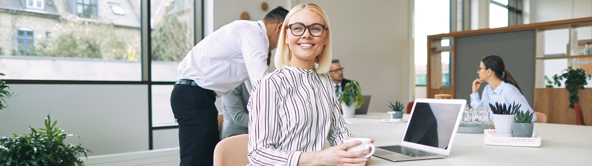 Lächelnde junge Frau sitzt mit Kaffeetasse an ihrem Arbeitsplatz