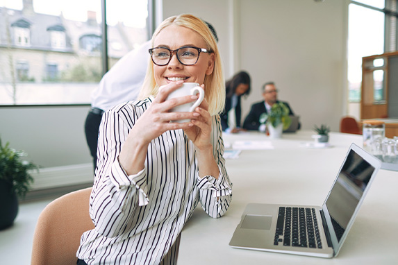 junge Frau sitzt mit Kaffeetasse vor einem Notebook