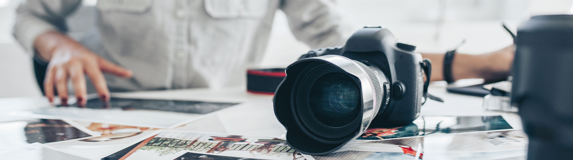 Bildausschnitt: Fotografin sichtet auf einem Tisch Fotos, Kamera liegt daneben