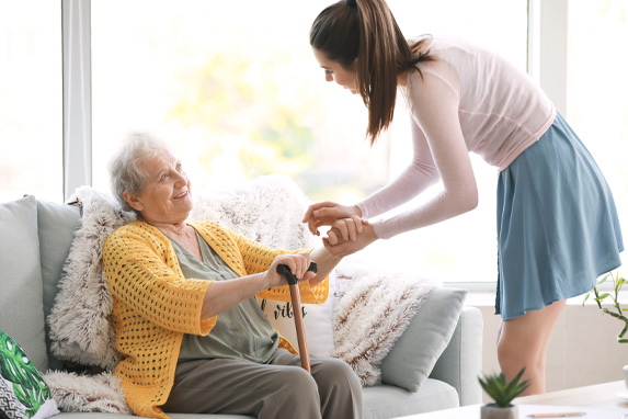 junge Frau beugt sich zu einer Seniorin auf einem Sofa