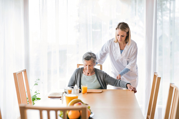 Junge Pflegerin hilft einer Seniorin am Esstisch