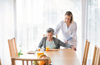 Interner Link zu der Seite: Pflegeeinrichtungen Junge Pflegerin hilft einer Seniorin am Esstisch