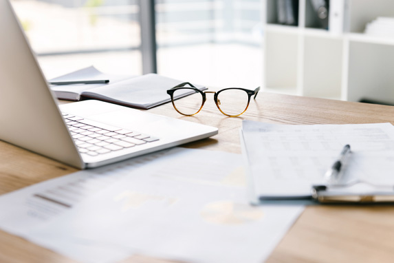 Arbeitsplatz mit Laptop, Brille und Schreibmaterial