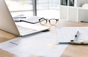 Arbeitsplatz mit Laptop, Brille und Schreibmaterial