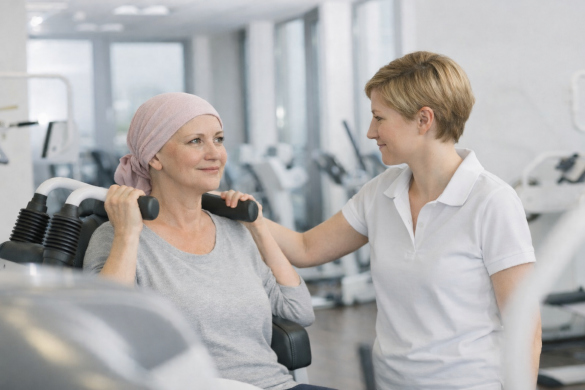 junge Frau mit Kopfbedeckung wird von einer Trainerin an einem Trainingsgerät angeleitet