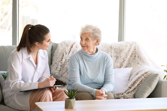 Ärztin im Gespräch mit einer Seniorin auf einem Sofa