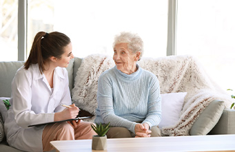 Ärztin im Gespräch mit einer Seniorin auf einem Sofa