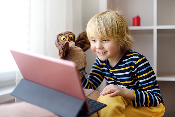 Kleiner, blonder Junge sitzt vor einem Tablet und spielt mit einer Plüscheule