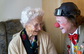 Älterer Clown mit roter Nase bringt Seniorin zum Lachen