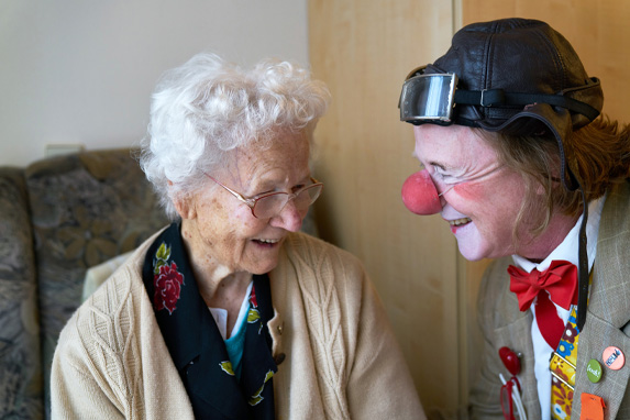 Älterer Clown mit roter Nase bringt Seniorin zum Lachen