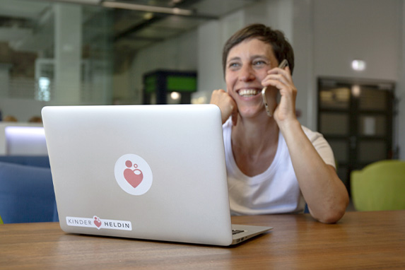 Junge Frau sitzt lächelnd vor einem Notebook und telefoniert