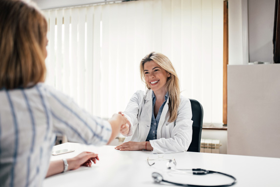 Lächelnde junge Ärztin gibt einer Patientin die Hand