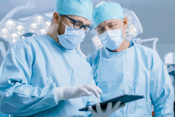 Zwei Ärzte in OP-Bekleidung blicken auf ein Tablet